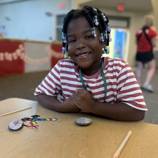 A young girl looking up from her work at the craft table.
