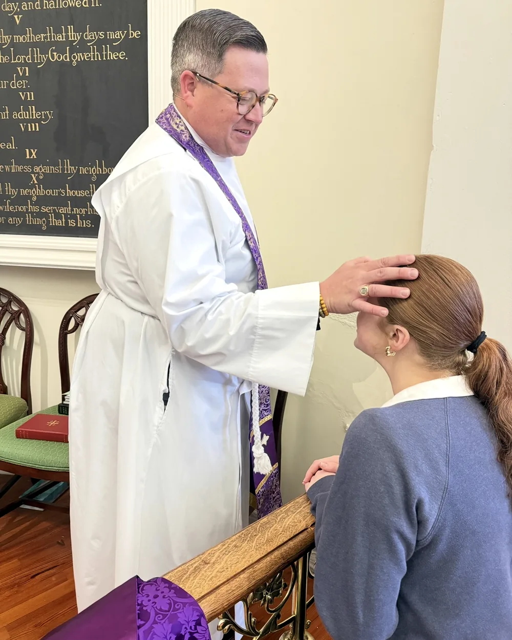 A priest laying hands in blessing on a parishioner kneeling at the altar rail.