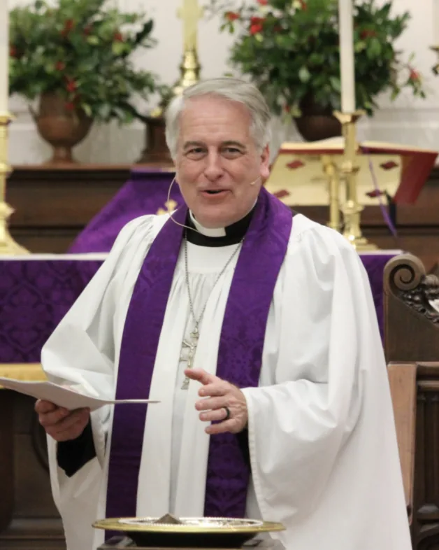 The Rector of St. Paul’s, in surplice and purple stole, speaking from the chancel steps with the altar behind him.
