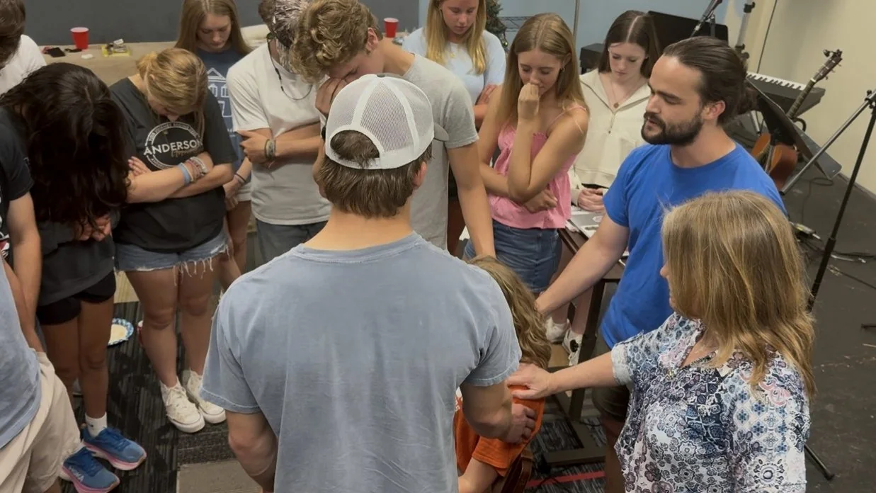 Young people and leaders at St. Paul’s standing in a close circle with heads bowed, hands laid on one another in prayer.