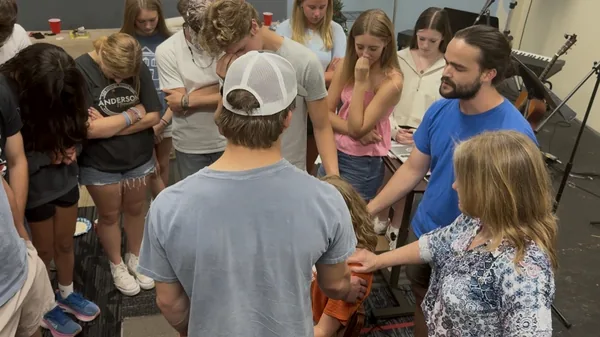 Young people standing shoulder to shoulder in prayer, hands reaching into the centre of the circle.